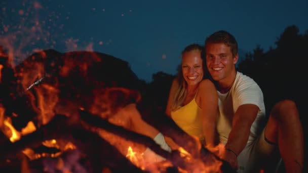 Slow Motion Freudiger Mann stochert am Lagerfeuer mit einem Ast, während er mit Mädchen kuschelt — Stockvideo