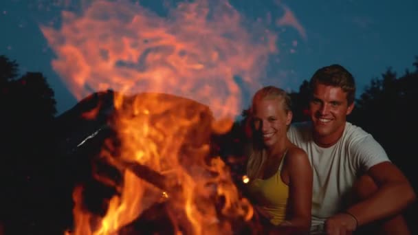 CLOSE UP: Excited woman laughs while her boyfriend pokes the campfire with stick — Stock Video