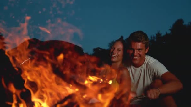 MOCIÓN LENTA: Mujer feliz riéndose mientras se acurruca con su novio junto al fuego . — Vídeo de stock