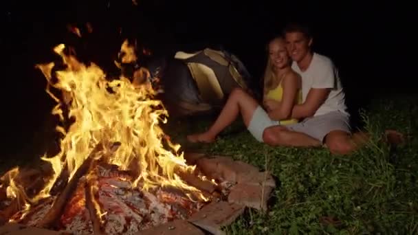 SLOW MOTION: Happy man kisses girlfriend on the cheek while cuddling by campfire — ストック動画