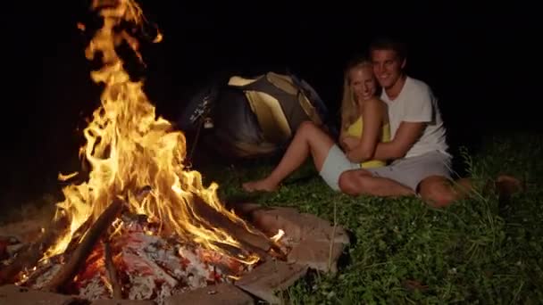 CLOSE UP: Cheerful Caucasian couple sits and cuddles by the warm campfire. — ストック動画