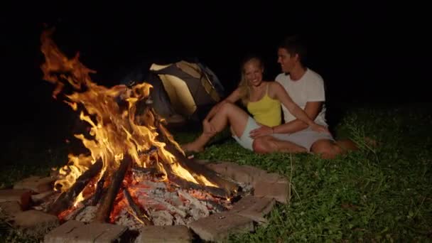 SLOW MOTION: Carefree couple camping in the wild laugh and kiss by the campfire. — ストック動画