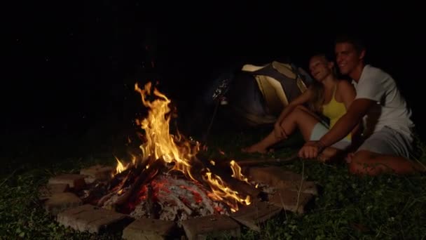 SLOW MOTION: Happy woman cuddling with boyfriend hitting the fire with a branch. — ストック動画