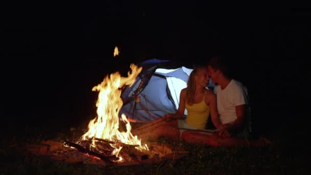 FERMER : Couple affamé câlinant près du feu de camp et rôtissant des saucisses la nuit . — Video