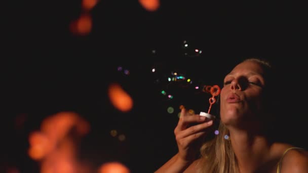 Slow Motion: Prachtige blanke vrouw blaast zeepbellen in de richting van het vuur. — Stockvideo
