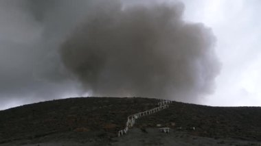 Beyaz korkuluklar ve izler Pasifik 'teki aktif bir volkanın tepesine çıkıyor..