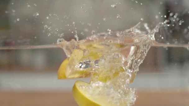 Slow Motion: Snijwonden van een rijpe gele appel vallen in het water en maken een plons — Stockvideo