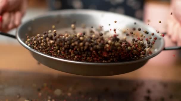 SLOW MOTION: Onherkenbare vrouw toasten kleurrijke peperkorrels in een metalen pan. — Stockvideo