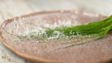 Uzun soğan sapları, soğuk suyla dolu sığ bir tabağa düşer..