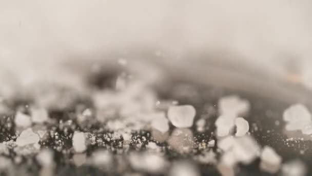 Witte kristallen van suiker stuiteren op het zwarte oppervlak van de keukentafel. — Stockvideo