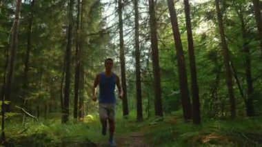 Enerjik atletik adam ormanın ortasından koşarak geçiyor..
