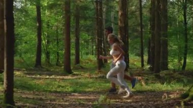 Neşeli sportif çift cennetlik çam ormanlarında koşuyor..