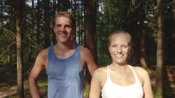 MOCIÓN LENTA: Los socios de entrenamiento sonrientes se paran frente a un bosque después de un trote . — Vídeo de stock