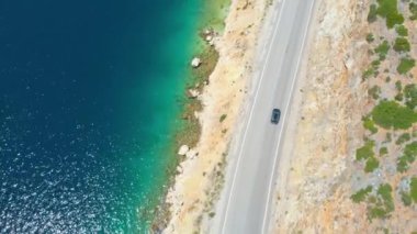 Lefkas 'ta güneşli bir günde manzaralı sahil yolunda ilerleyen gri araba.