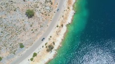 Koyu gri araba güneşli bir yaz gününde Lefkas kıyılarında yol alıyor.