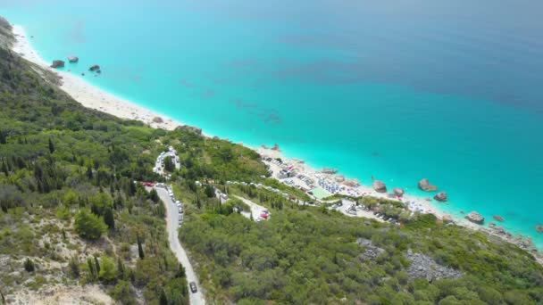AERIAL: Voando acima da estrada costeira com vista para a praia lotada em Lefkada. — Vídeo de Stock