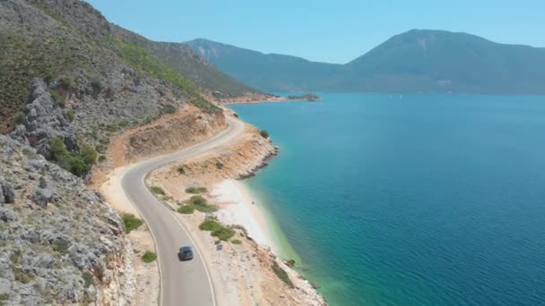 AERIAL: Γκρι αυτοκίνητο οδήγηση κατά μήκος της όμορφης ακτογραμμής ενός γραφικού απομακρυσμένου νησιού — Αρχείο Βίντεο