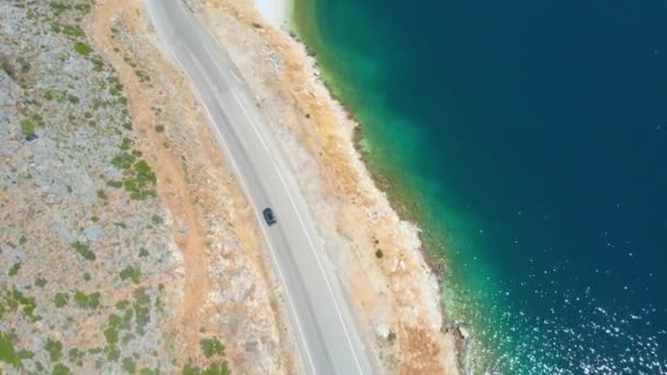 AERIAL: mélykék óceán ragyog, miközben az autó cirkál a festői úton. — Stock videók