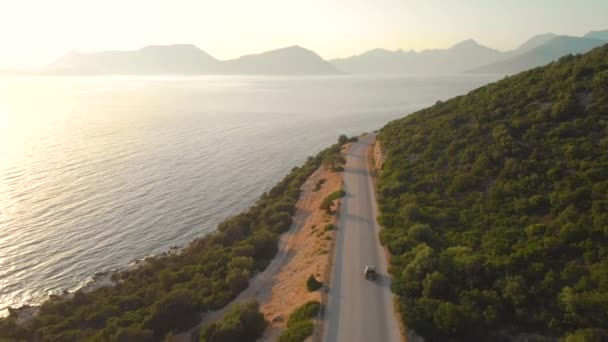 DRONE: Voando atrás do carro turístico que dirige para baixo a estrada vazia que conduz em torno da ilha. — Vídeo de Stock
