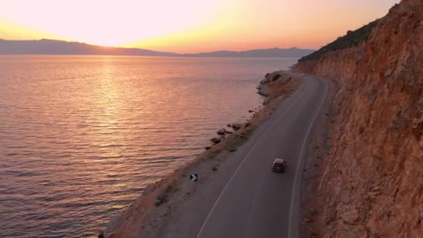 AERIAL: Människor på sommaren road trip kryssning längs stenig strand vid soluppgången. — Stockvideo