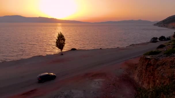 DRONE: Goldener Sonnenuntergang beleuchtet das Meer und das Auto, das auf der malerischen Straße fährt. — Stockvideo