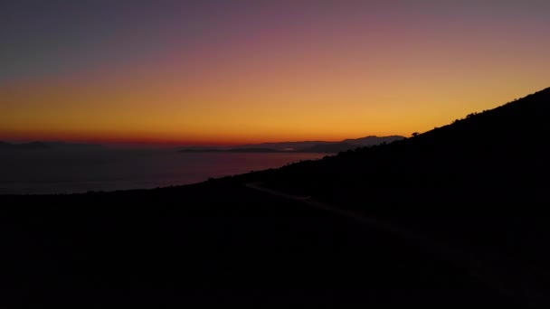 Auto verdwijnt in de verte terwijl hij rond Lefkas rijdt bij zonsondergang.. — Stockvideo