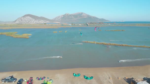 DRONE: Πολύχρωμο χαρταετούς τραβώντας kitesurfers γύρω από θυελλώδη κόλπο σε μια ηλιόλουστη μέρα του καλοκαιριού — Αρχείο Βίντεο