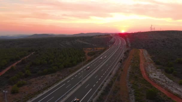 AERIAL: Kolorowy zachód słońca oświetla autostradę biegnącą przez spokojną okolicę. — Wideo stockowe