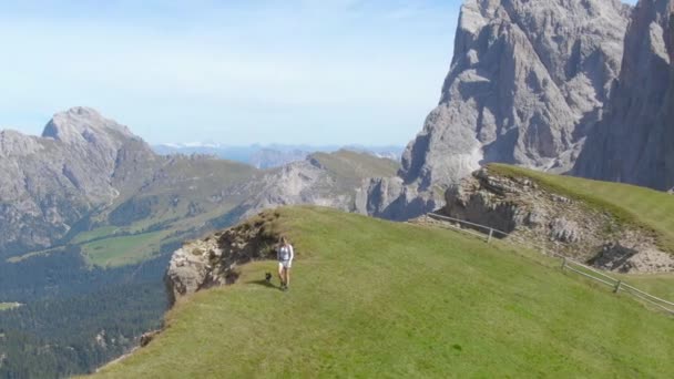 AERIAL: Mujer activa y su cachorro negro caminan a lo largo de la cima de la montaña cubierta de hierba . — Vídeos de Stock