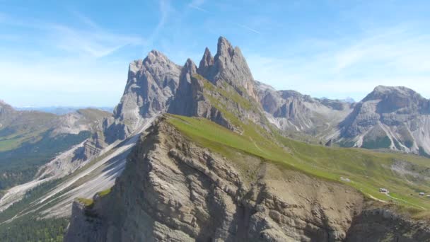 AERIAL: Adembenemende opname van een grazige heuvel onder de majestueuze rotsachtige bergen. — Stockvideo