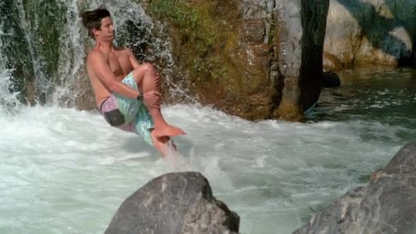 SLOW MOTION: Cheerful man jumps off edge of a waterfall and does a cannonball. — Stock Video