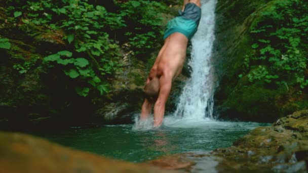 Nah am Fluss plätschert das Wasser, als der sportliche Tourist kopfüber in einen Teich springt — Stockvideo