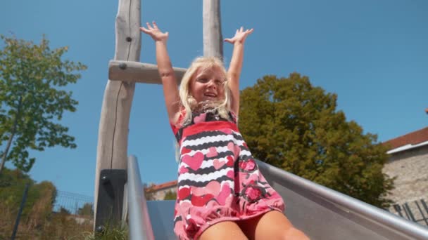 慢动作：一个快乐的小女孩在操场上玩耍，滑倒在滑梯上 — 图库视频影像