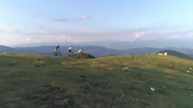 Bir grup arkadaş dağ bisikletleriyle çimenli bir tepeden aşağı doğru hızla ilerliyorlar..