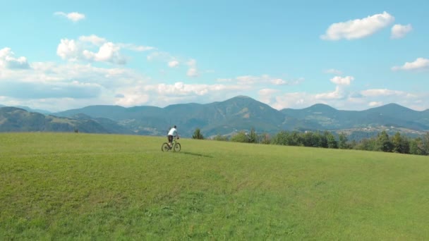 AERIAL: Fit man downhill biking across an empty meadow in Slovenian mountains. — Stock Video