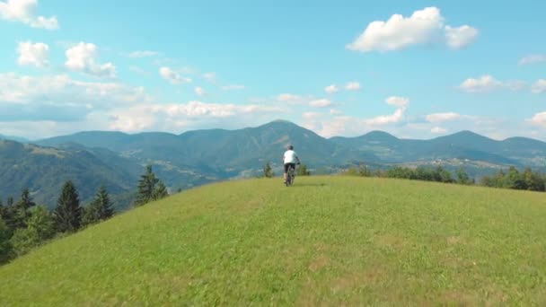 Volando detrás de un hombre irreconocible montando su bicicleta de montaña a través de un prado — Vídeo de stock