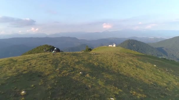 AERIAL: Horští cyklisté rychlost podél malebné stezky vedoucí přes travnatý kopec. — Stock video