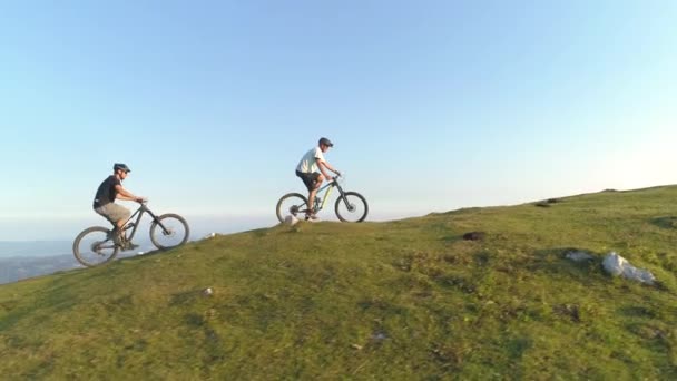 DRONE: Dva horští cyklisté jezdí na elektrických kolech do strmého travnatého kopce. — Stock video