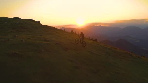 Şafakta çimenli bir tepede elektrikli bisiklete binen bir adam boyunca uçmak.. — Stok video