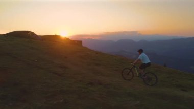 Dağ bisikletçisi resimli günbatımında çimenli bir tepede bisikletini sürüyor.