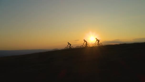 AERIAL: Golden sunbeams shine on friends downhill biking at picturesque sunset. — Stock Video