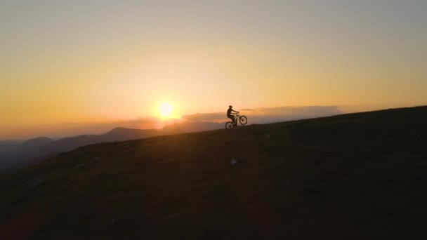 SILHOUETTE: El hombre que monta una bicicleta de montaña hace un wheelie mientras que monta cuesta arriba . — Vídeos de Stock