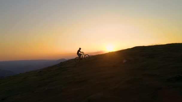 DRONE: Unrecognizable cyclist rides an electric bike uphill at golden sunset. — Stock Video