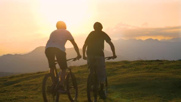 Três amigos montam suas bicicletas até a borda de uma colina e cinco ao pôr do sol. — Vídeo de Stock