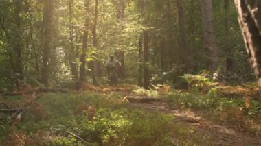 Yokuş aşağı aşırı bisiklet yarışçısı toprak yoldaki bir kütüğün üzerinden geçiyor.