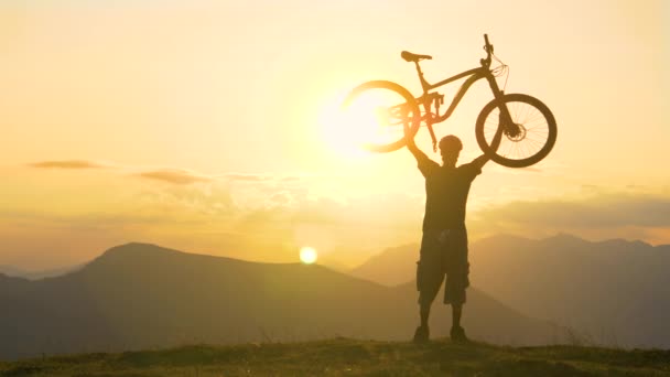 Молодий велосипедист тримає велосипед над головою на золотому заході сонця . — стокове відео