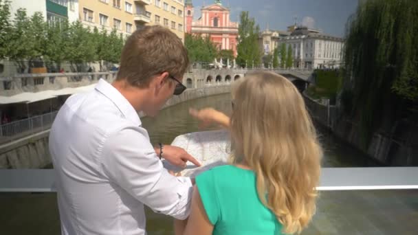 SLOW MOTION Couple regardant une carte et pointant vers des bâtiments ensoleillés Ljubljana — Video