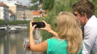 Tanımlanamayan sarışın kadın akıllı telefonuyla nehrin fotoğraflarını çekiyor.
