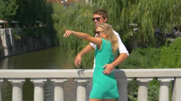 SLOW MOTION: Νεαρό ζευγάρι ερωτευμένων ταξιδιωτών διασχίζει μια γέφυρα στη Λιουμπλιάνα. — Αρχείο Βίντεο