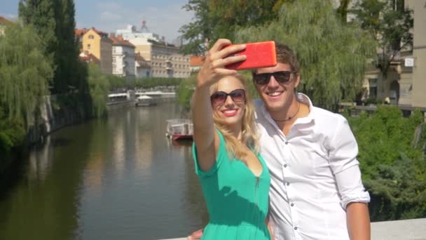 SLOW MOTION: Χαρούμενα ταξιδιώτες παίρνουν selfies από μια γέφυρα στην ηλιόλουστη Λιουμπλιάνα. — Αρχείο Βίντεο